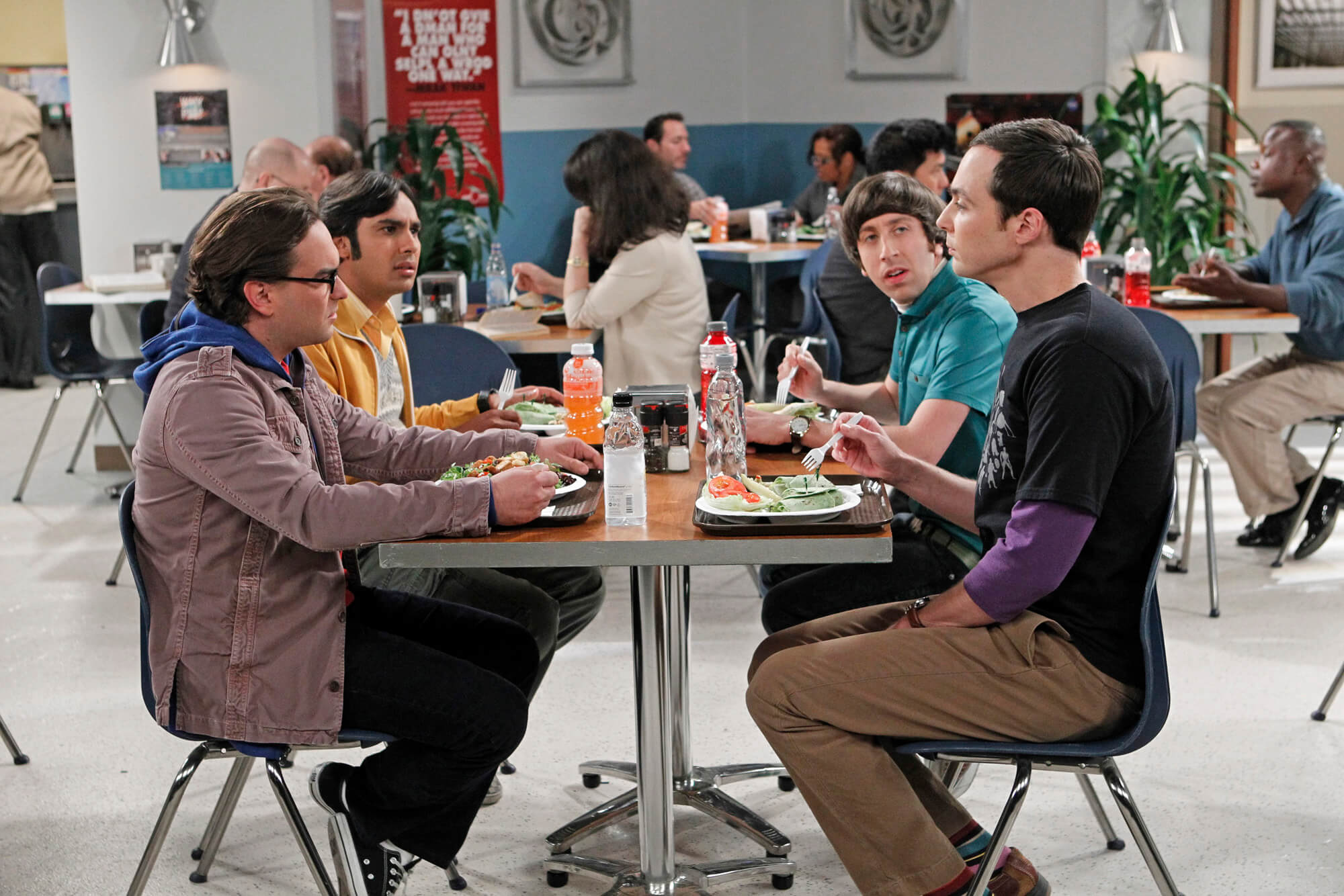 Four men sitting at a table in a cafeteria, having a conversation over lunch